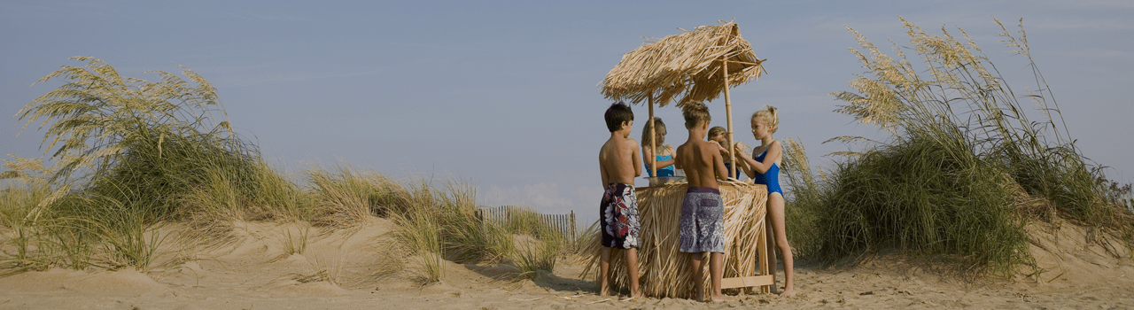 A group of young people standing around an outdoor tiki bar.