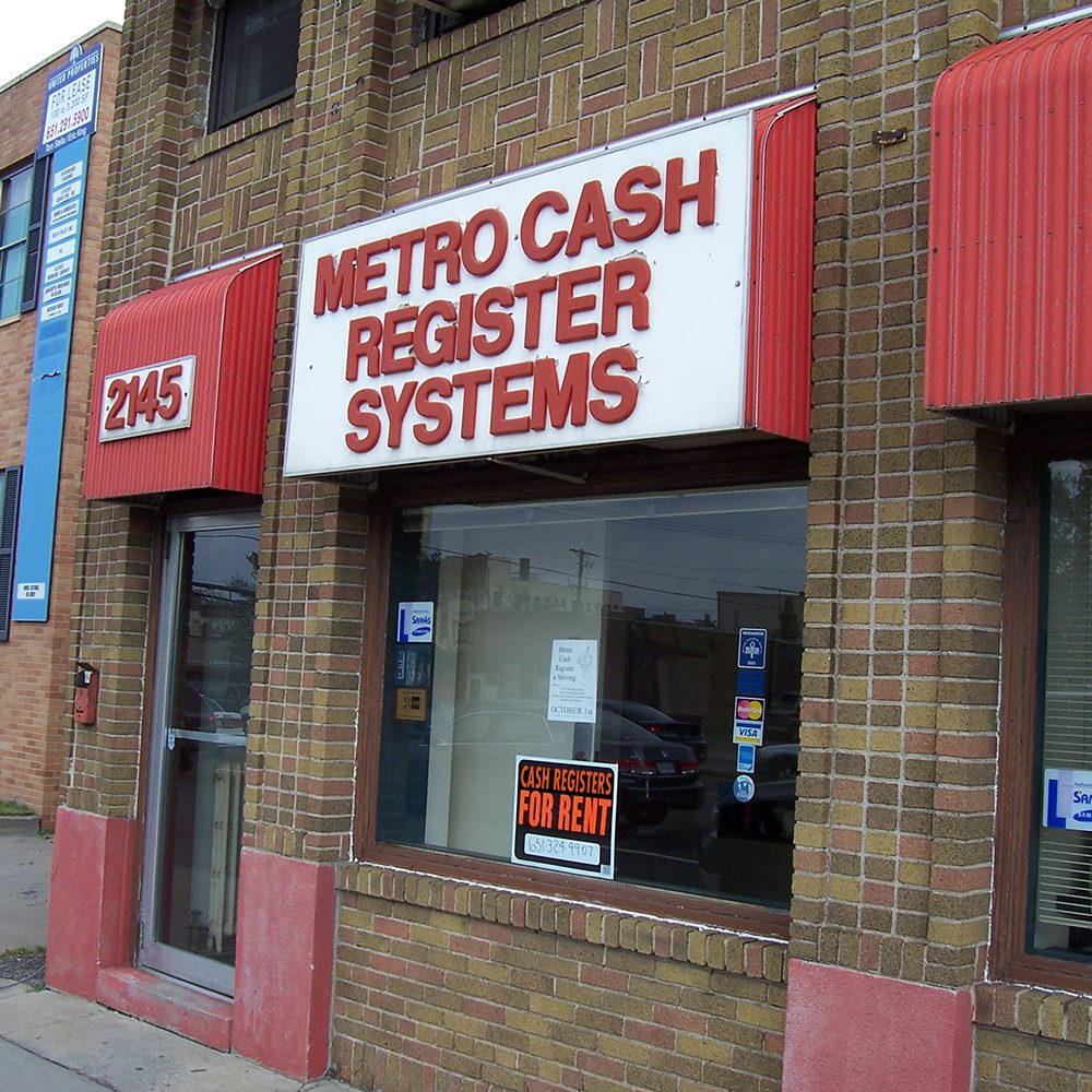 Exterior of metro cash register systems store with red awnings and signs advertising cash registers for sale and rent.