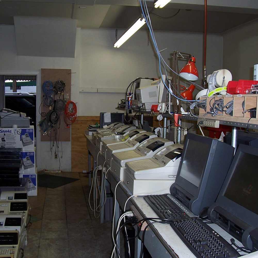 An electronics workshop with various disassembled computers and peripherals on a counter, surrounded by tools and equipment.