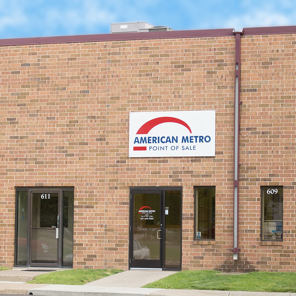 Exterior of a one-story brick building with "american metro point of sale" sign above two glass doors, numbered 611 and 609, under a clear sky.