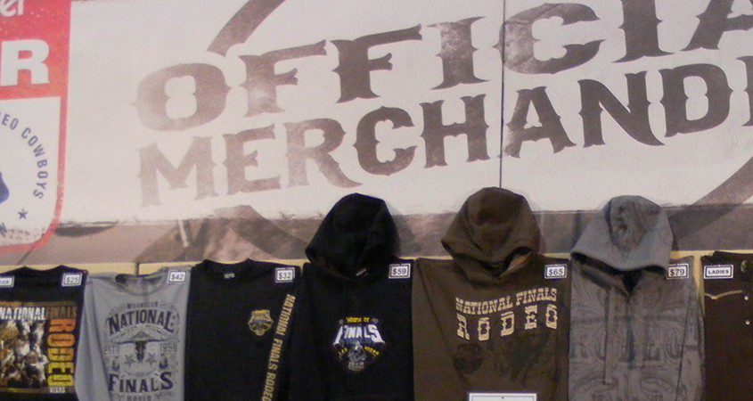 Row of merchandise including t-shirts and hooded sweatshirts displayed on a wall under a sign reading "official merchandise.
