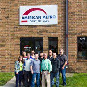 A group of nine people standing in front of a brick building with a sign that reads "american metro point of sale.