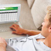 Man reclining on a couch, using a laptop with a spreadsheet open.