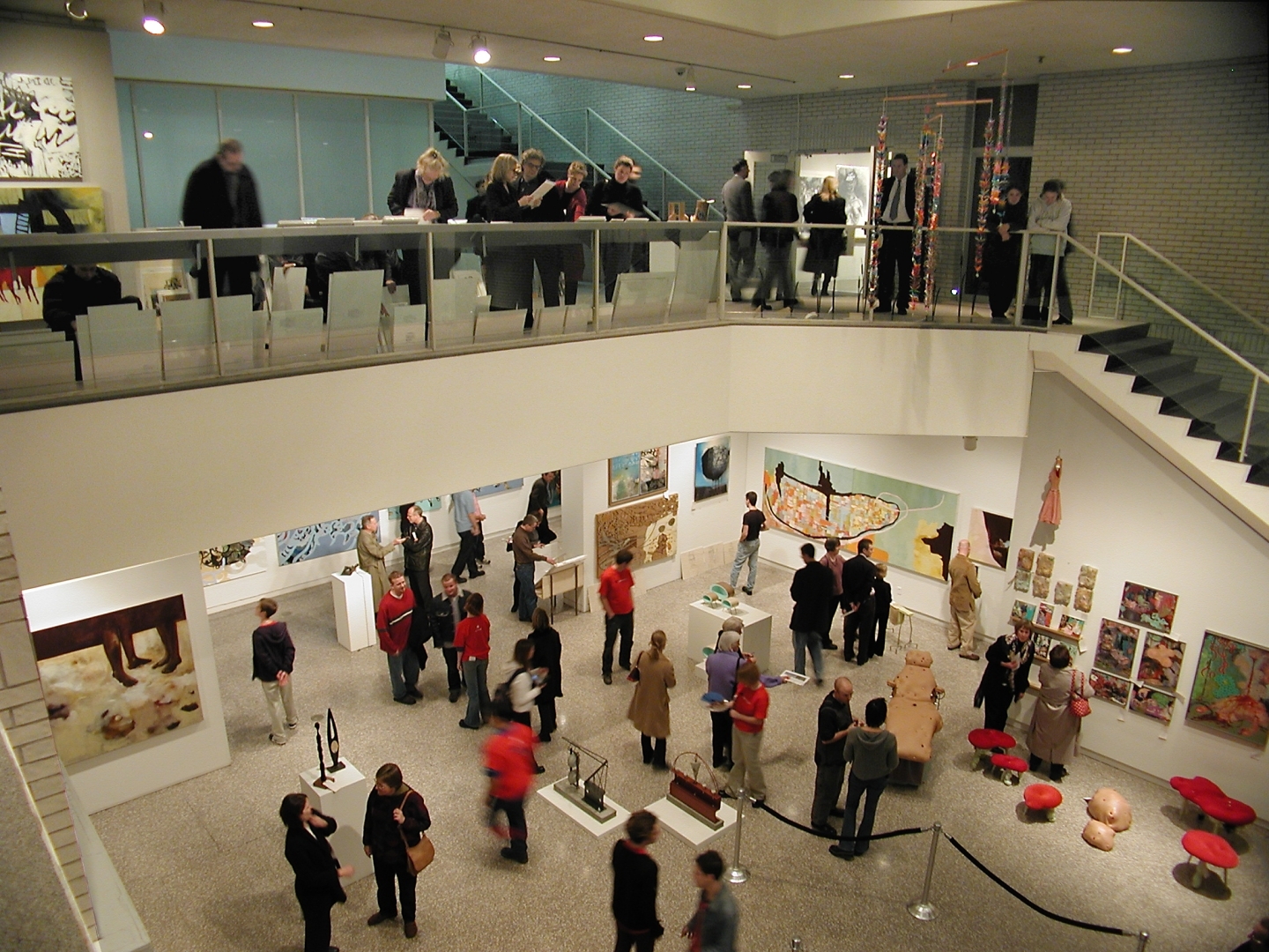 People viewing art exhibits in a multi-level gallery with balconies and staircases.