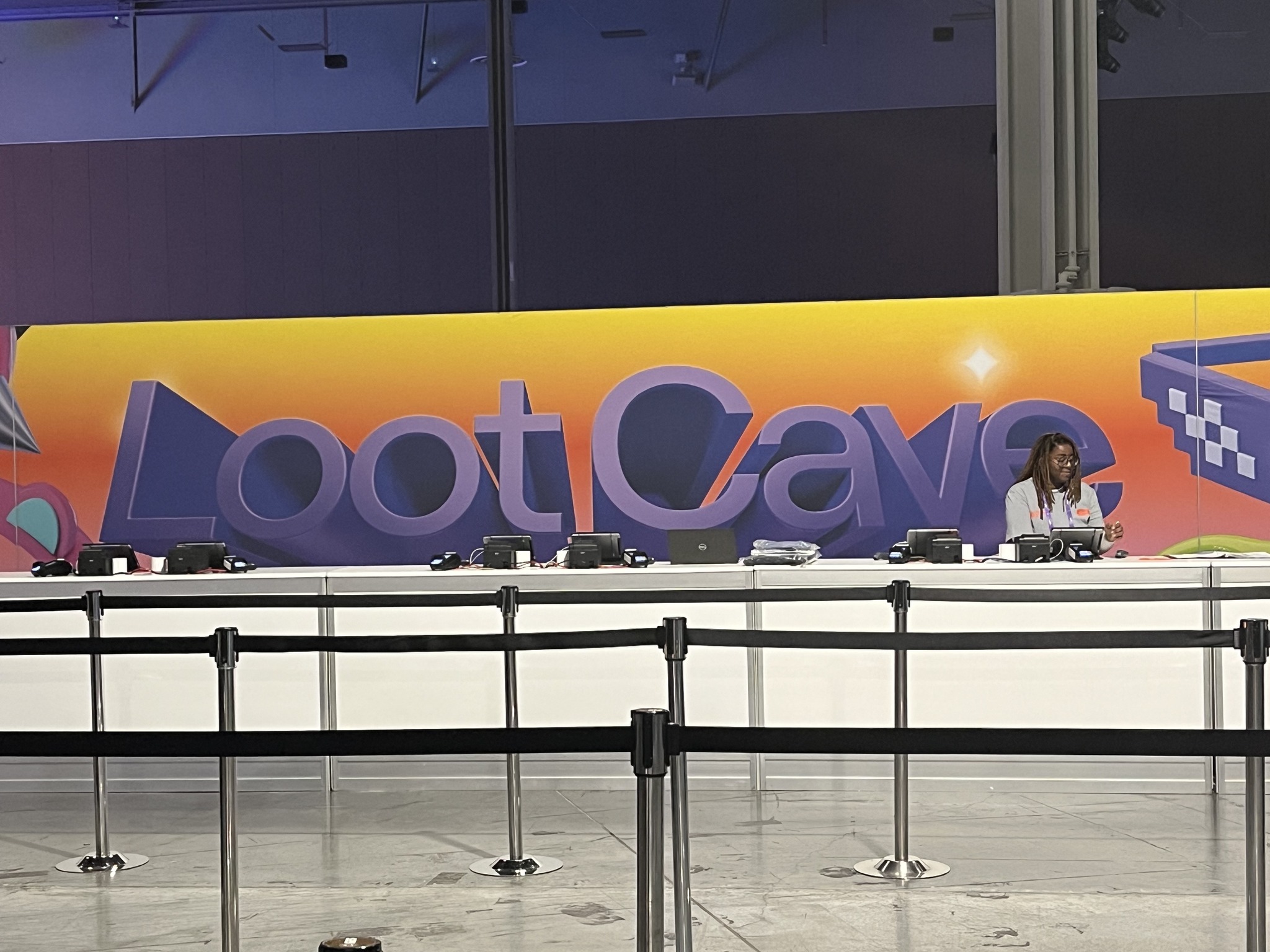 A woman staffs a registration desk labeled "loot cave" in a colorful, modern event hall.