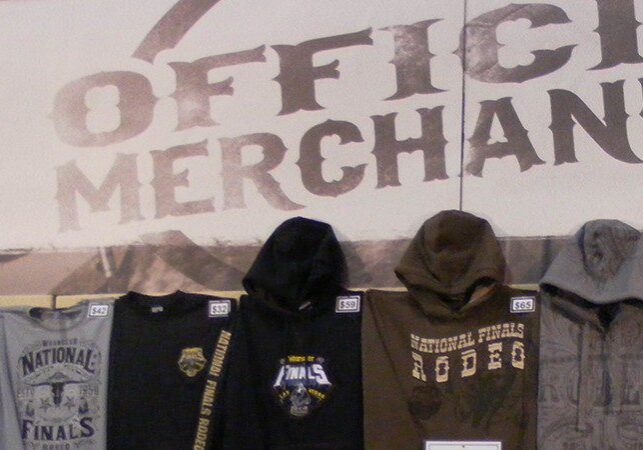 Row of merchandise including t-shirts and hooded sweatshirts displayed on a wall under a sign reading "official merchandise.