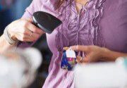 Woman in a purple blouse using a barcode scanner on a small product in a retail environment.