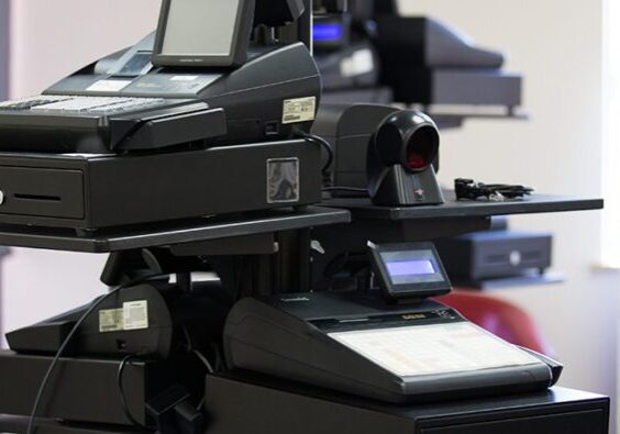 A row of modern electronic cash registers and point of sale systems on a counter in an office supply store.